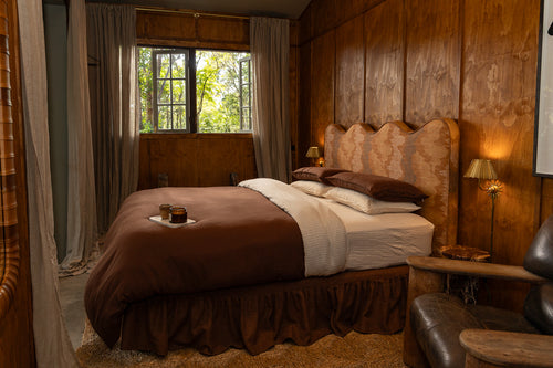 A neatly made NESTD bed styled with rich Sable brown pillows and a folded duvet over Canyon white striped sheets.