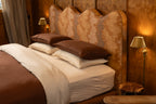 A neatly made NESTD bed styled with rich Sable brown pillows and a folded duvet over Canyon white striped sheets.