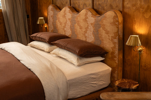A neatly made NESTD bed styled with rich Sable brown pillows and a folded duvet over Canyon white striped sheets.