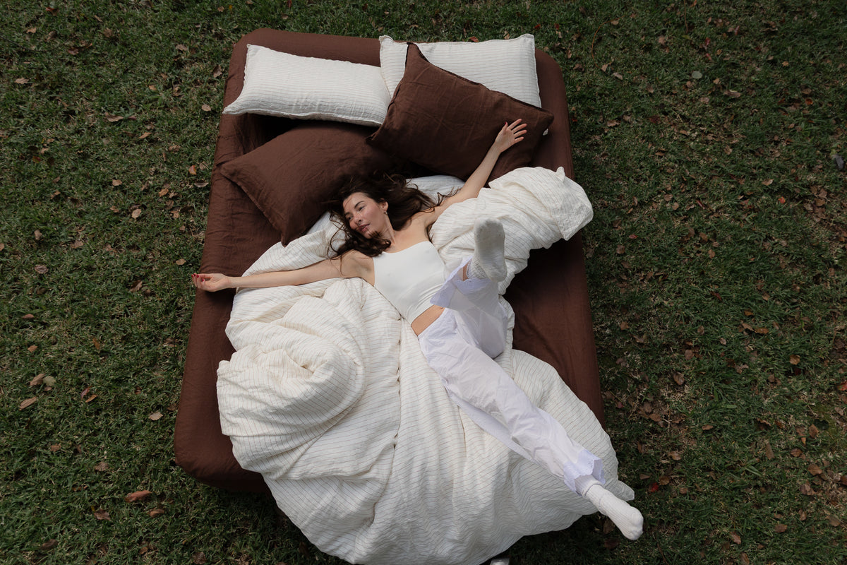 Woman in lying on a sable and canyon sheets set bed on grass.