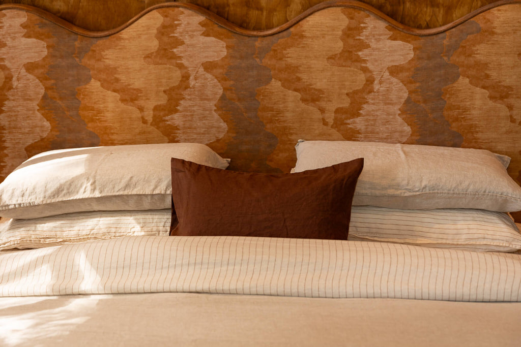 NESTD luxury flax linen bedding featuring Canyon and Dune white layers, styled with matching pillows and a draped duvet against a warm textured headboard.
