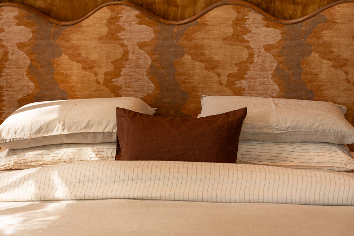 NESTD luxury flax linen bedding featuring Canyon and Dune white layers, styled with matching pillows and a draped duvet against a warm textured headboard.