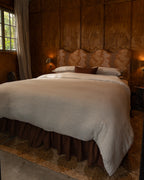 NESTD luxury flax linen bedding featuring Canyon and Dune white layers, styled with matching pillows and a draped duvet against a warm textured headboard.