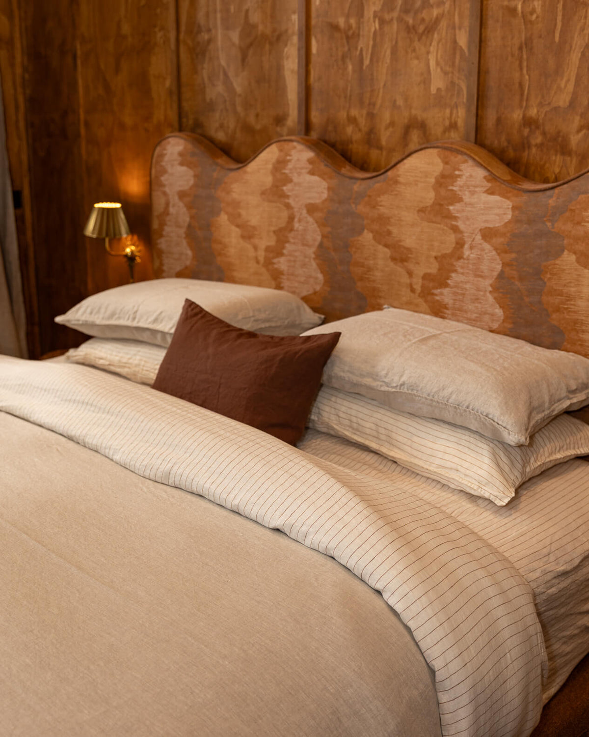 NESTD luxury flax linen bedding featuring Canyon and Dune white layers, styled with matching pillows and a draped duvet against a warm textured headboard.