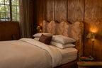 NESTD luxury flax linen bedding featuring Canyon and Dune white layers, styled with matching pillows and a draped duvet against a warm textured headboard.