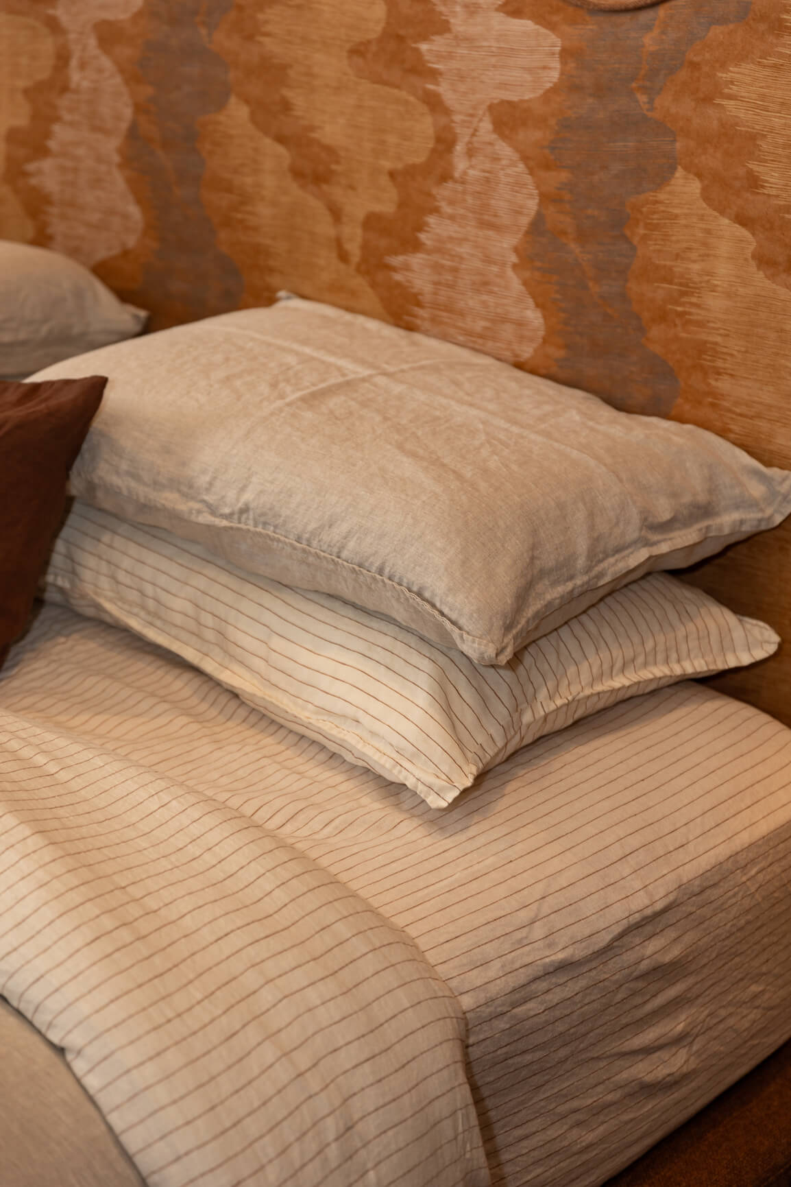 NESTD luxury flax linen bedding featuring Canyon and Dune white layers, styled with matching pillows and a draped duvet against a warm textured headboard.
