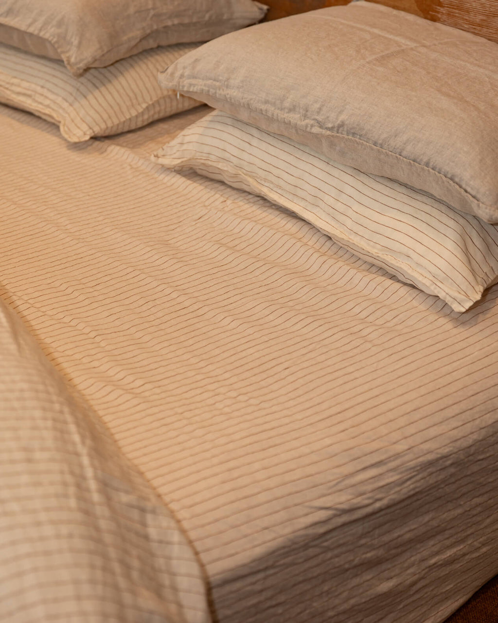 NESTD luxury flax linen bedding featuring rich Canyon and Dune white layers, styled with matching pillows and a draped duvet against a warm textured headboard.