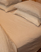 NESTD luxury flax linen bedding featuring rich Canyon and Dune white layers, styled with matching pillows and a draped duvet against a warm textured headboard.