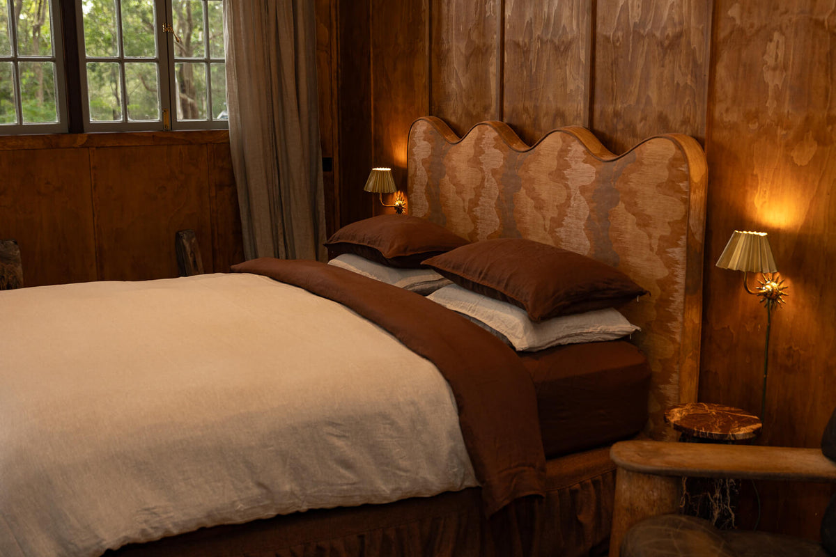 Cozy bedroom with wooden walls and a NESTD luxury flax linen bedding featuring rich Sable brown and Dune layers, styled with matching pillows and a draped duvet against a warm textured headboard.