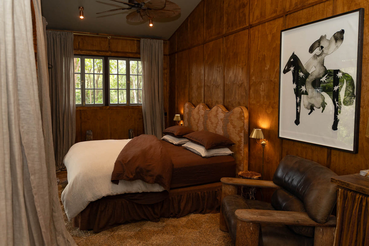 Cozy bedroom with wooden walls and a NESTD luxury flax linen bedding featuring rich Sable brown and Dune layers, styled with matching pillows and a draped duvet against a warm textured headboard.